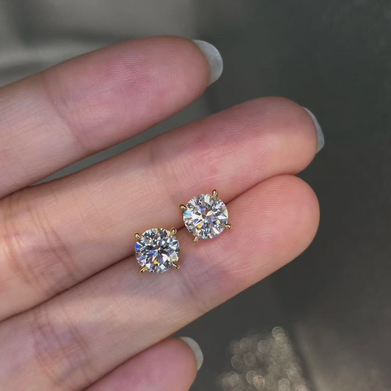Round brilliant lab diamond stud earrings held on fingertips - close up sparkle