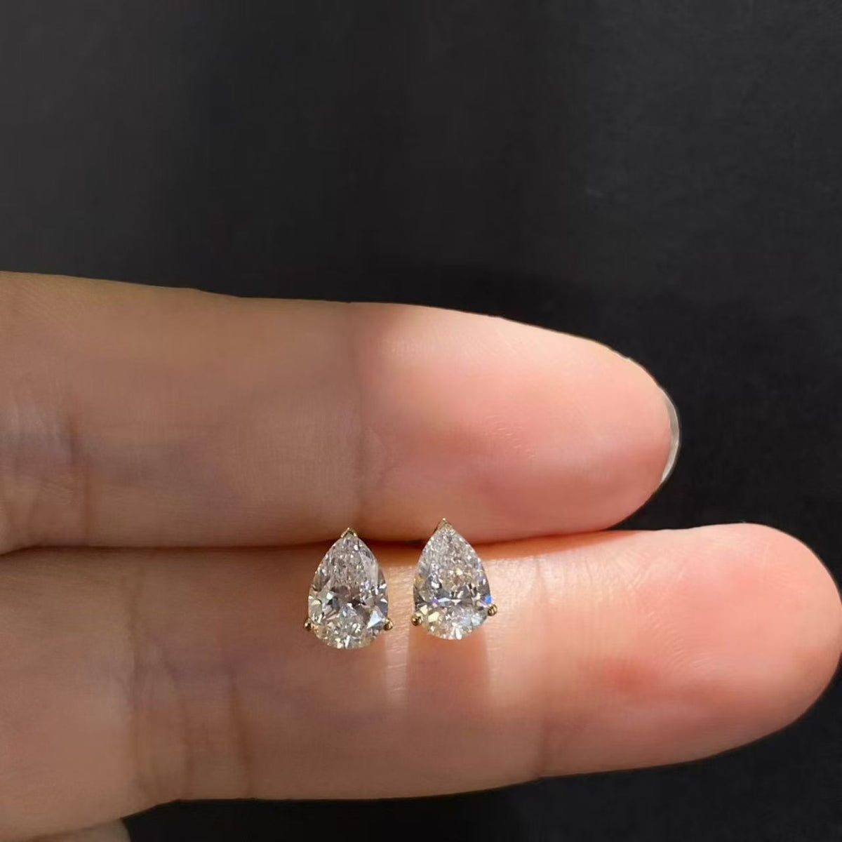 Pear solitaire lab diamond stud earrings held on fingertip - front view