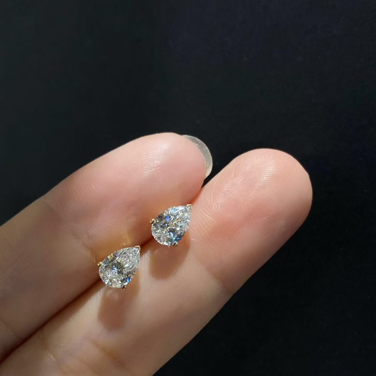 Pear solitaire lab diamond stud earrings held on fingertip - angle view