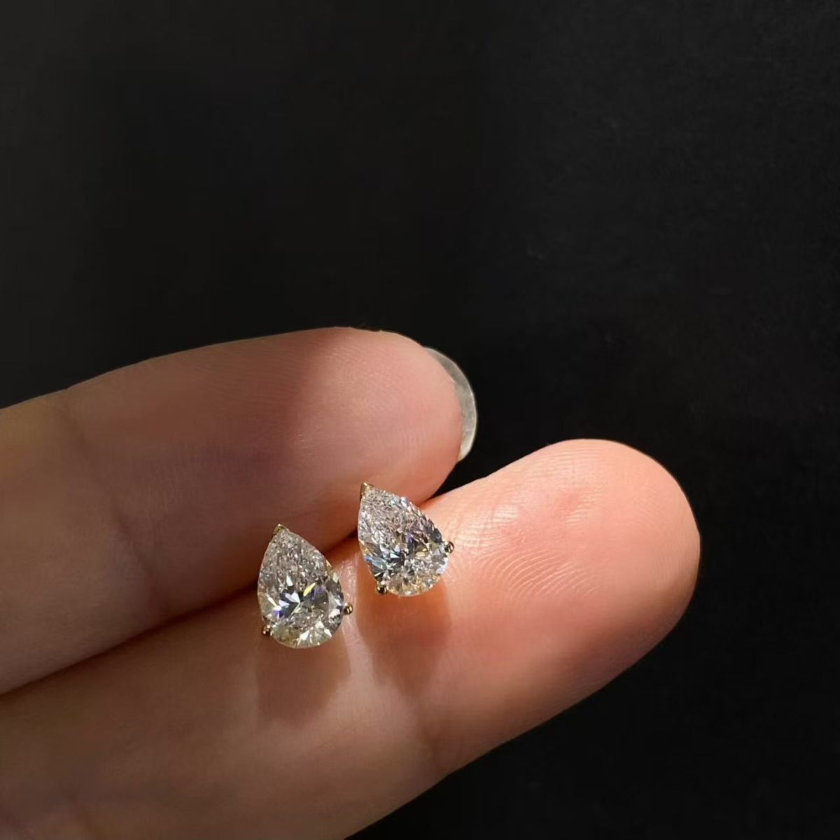 Pear solitaire lab diamond stud earrings held on fingertip - close up