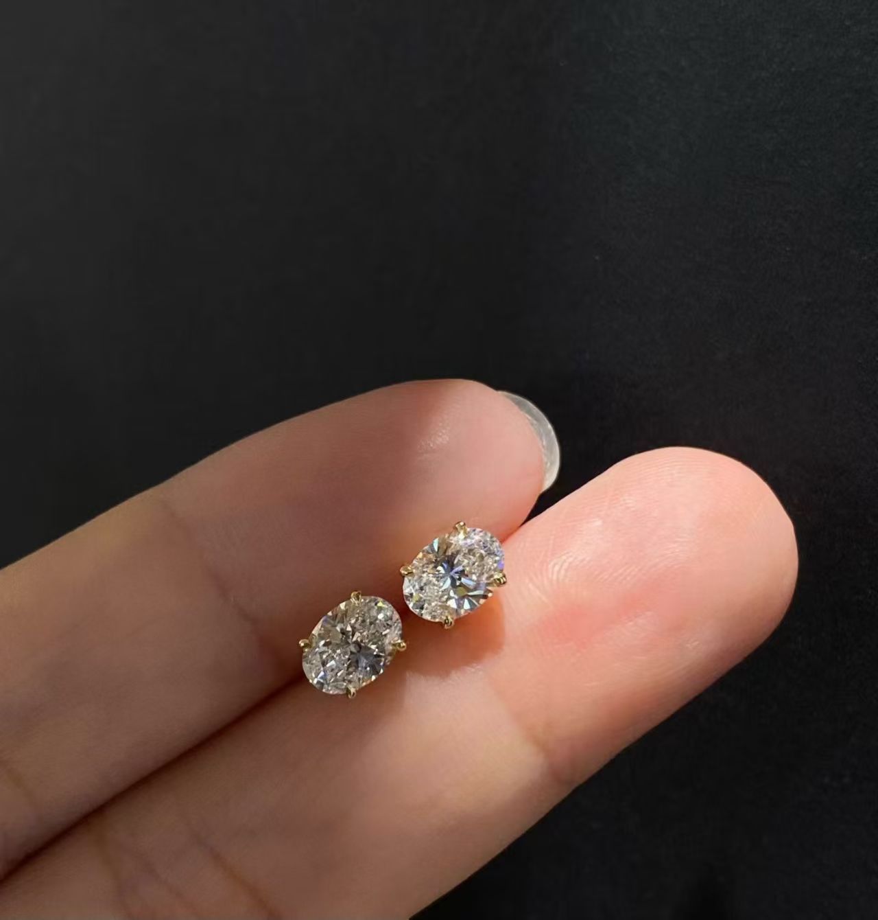 Oval solitaire lab diamond stud earrings held on fingertips - close up