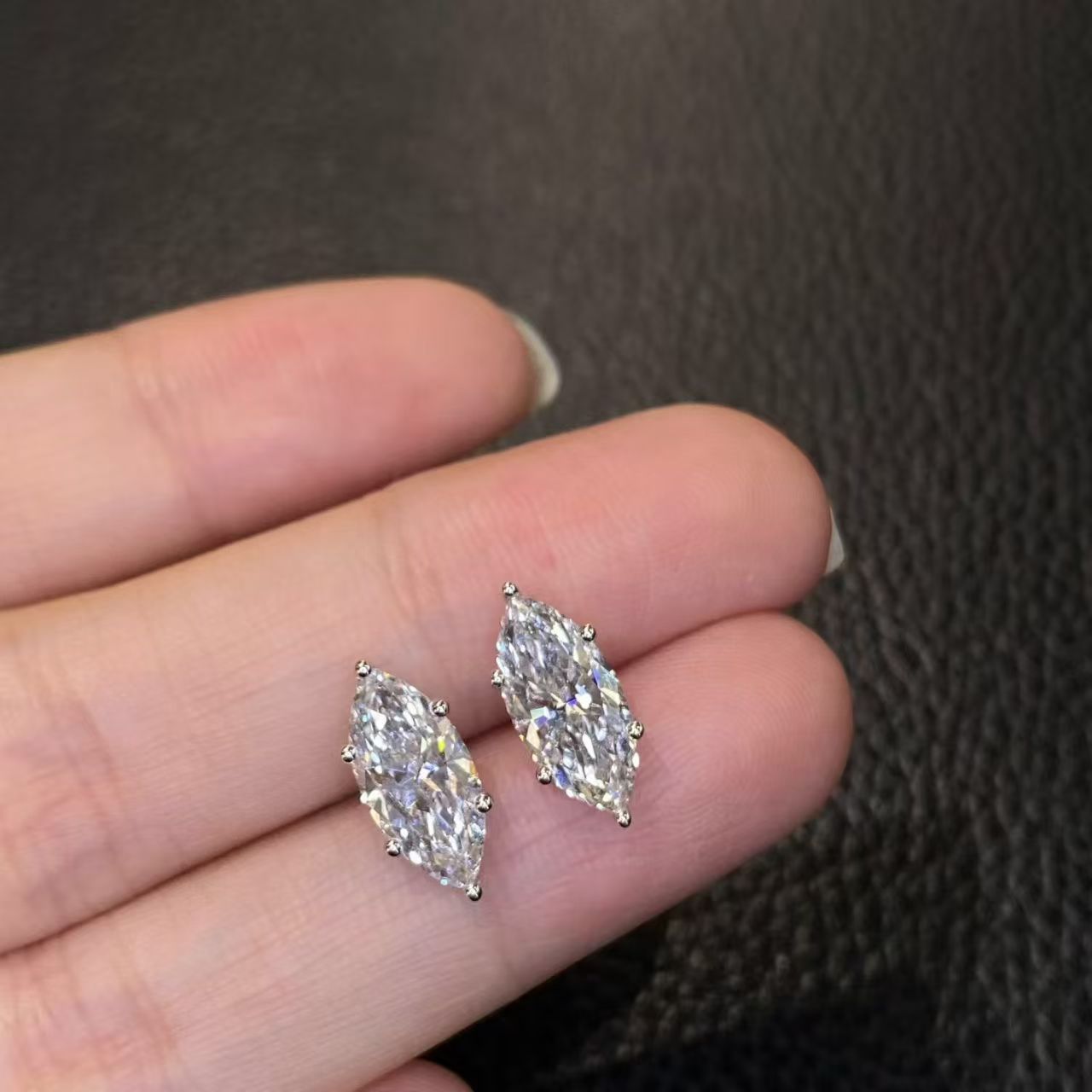 Marquise solitaire lab diamond stud earrings held on fingertip - front view