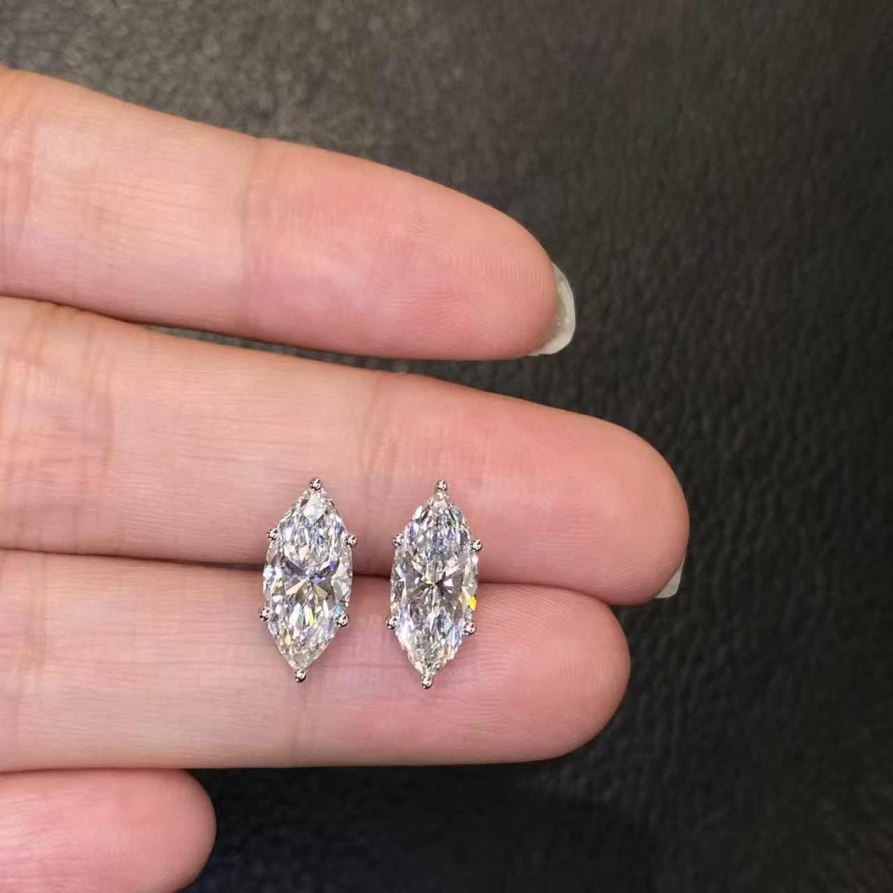 Marquise solitaire lab diamond stud earrings held on fingertip - close up