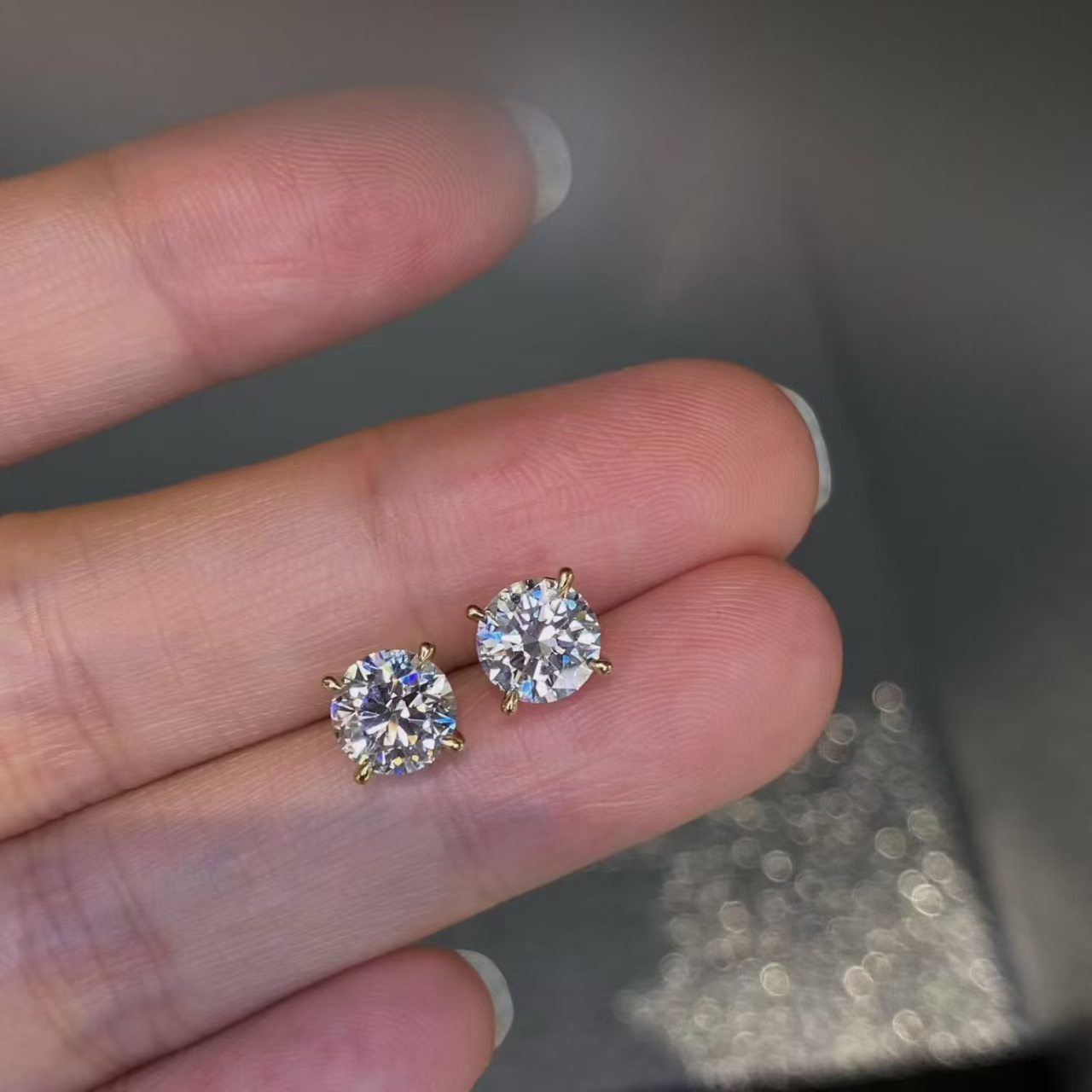 Round brilliant lab diamond stud earrings held on hand - size comparison view