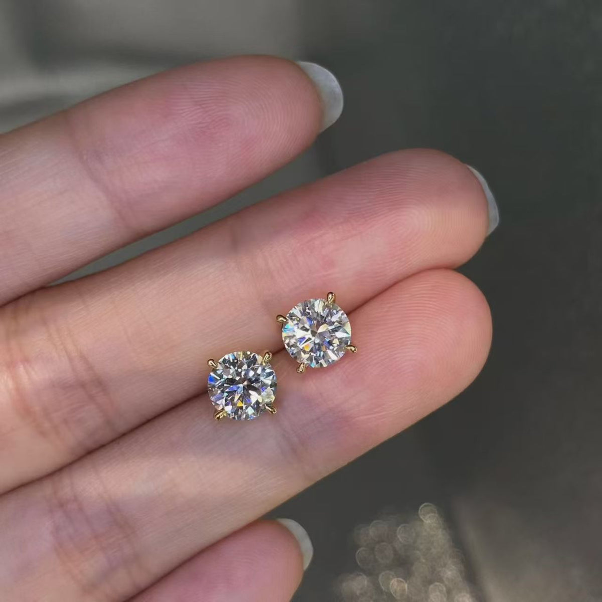 Round brilliant lab diamond stud earrings held on fingertips - close up sparkle