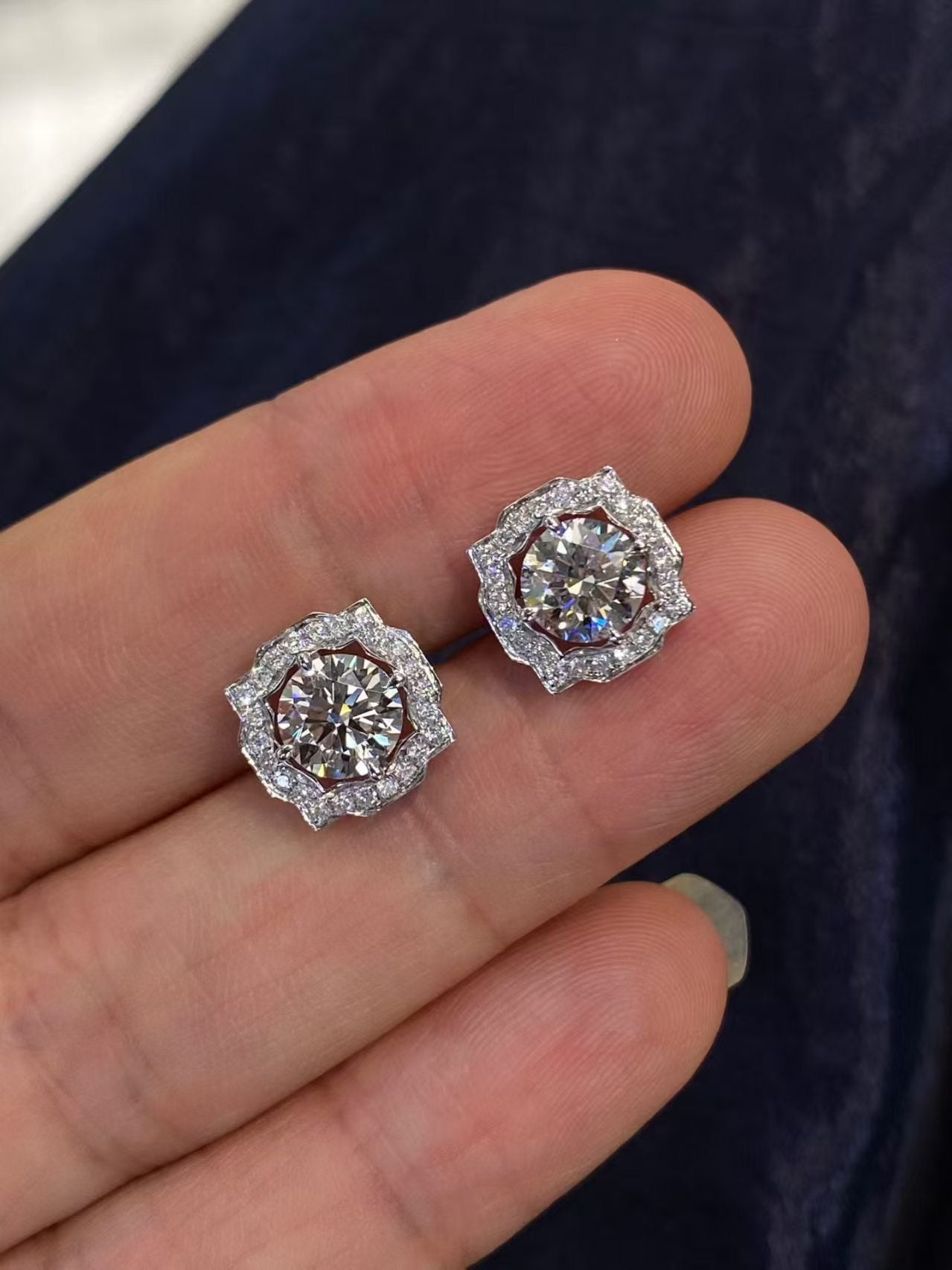 Round brilliant halo lab diamond stud earrings held on fingertips - close up angle view